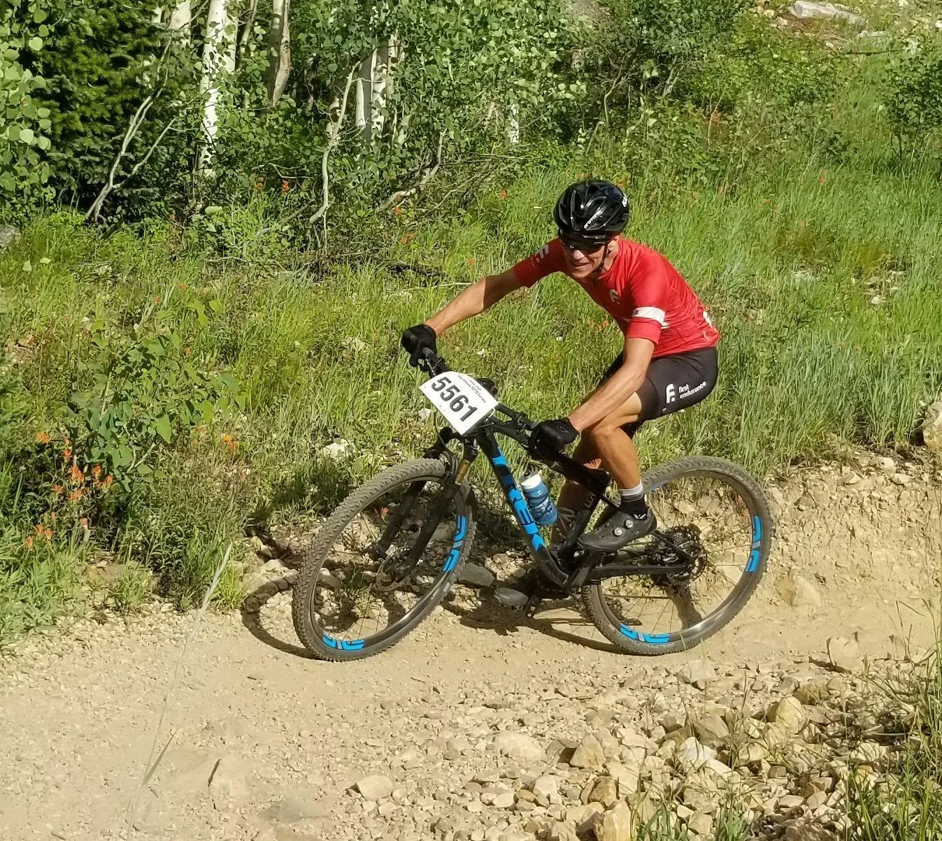 Mountain biker in a red jersey rounding a dusty turn beside aspen trees