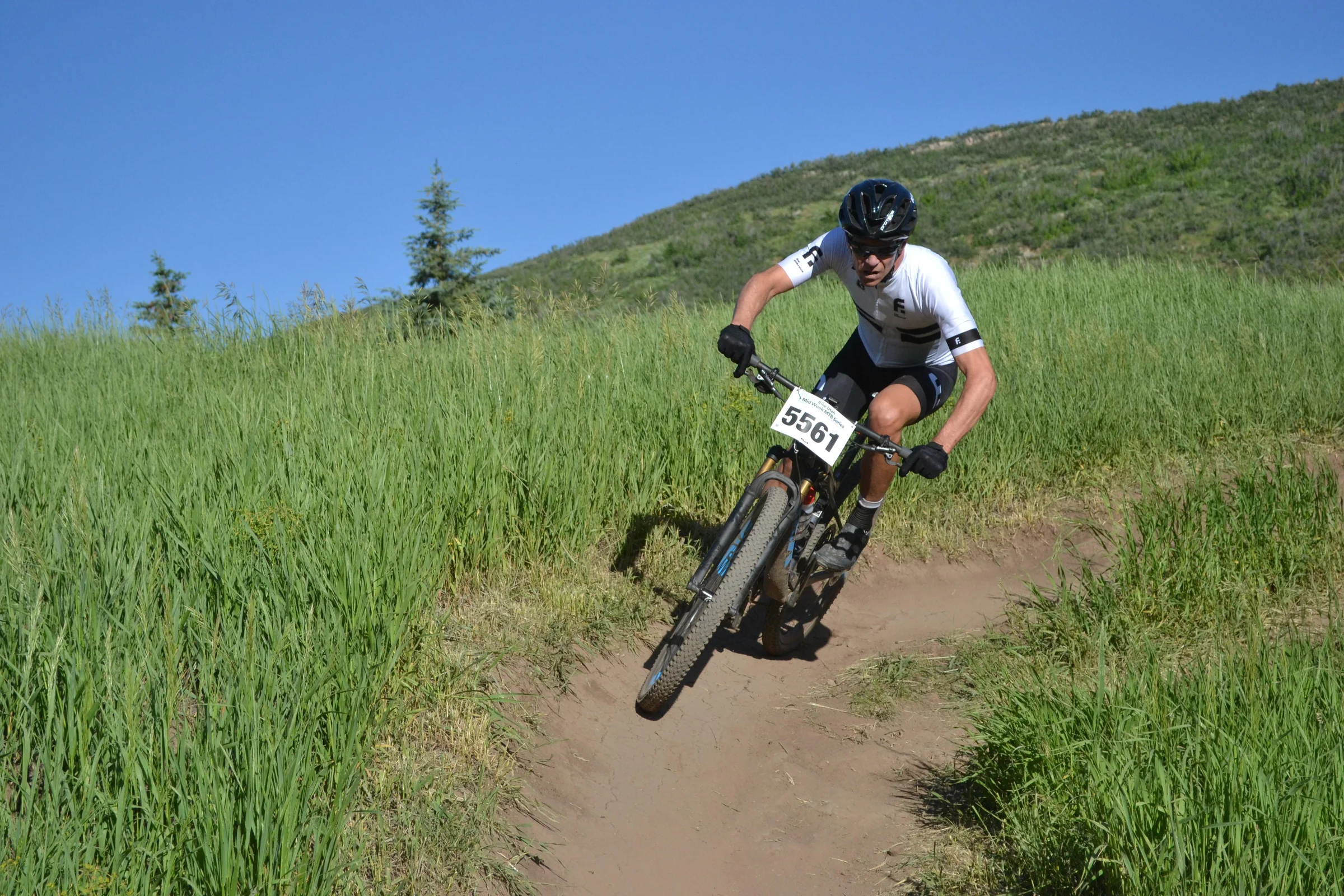 Mountain biker in a white jersey leaning through a turn on a grassy hillside