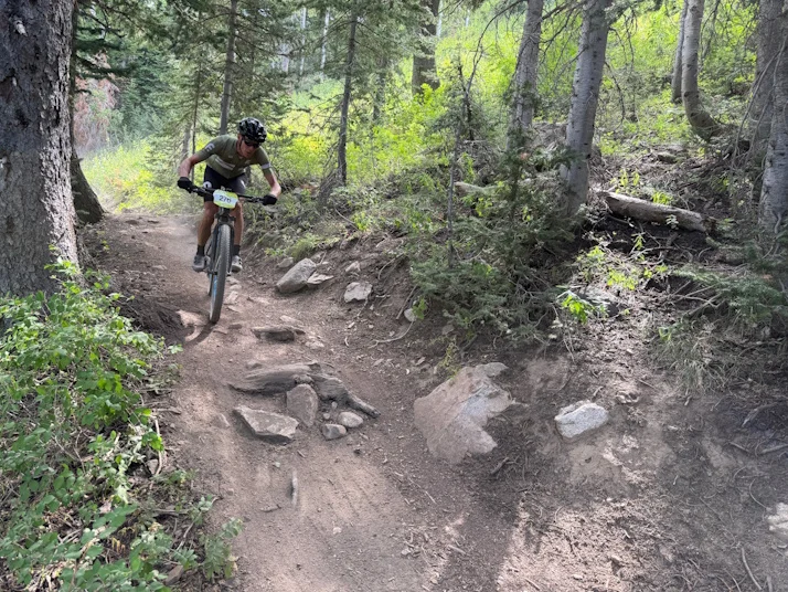 Mountain biker riding a rocky trail through a green forest